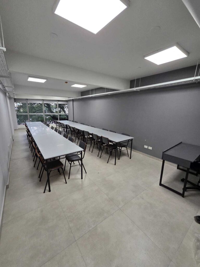 Sala de conferencias moderna con mesas largas y sillas negras. Espacio para la Experiencia.