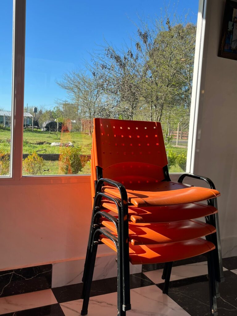 Sillas naranjas apiladas junto a la ventana con vista al jardín. Experiencia visual.
