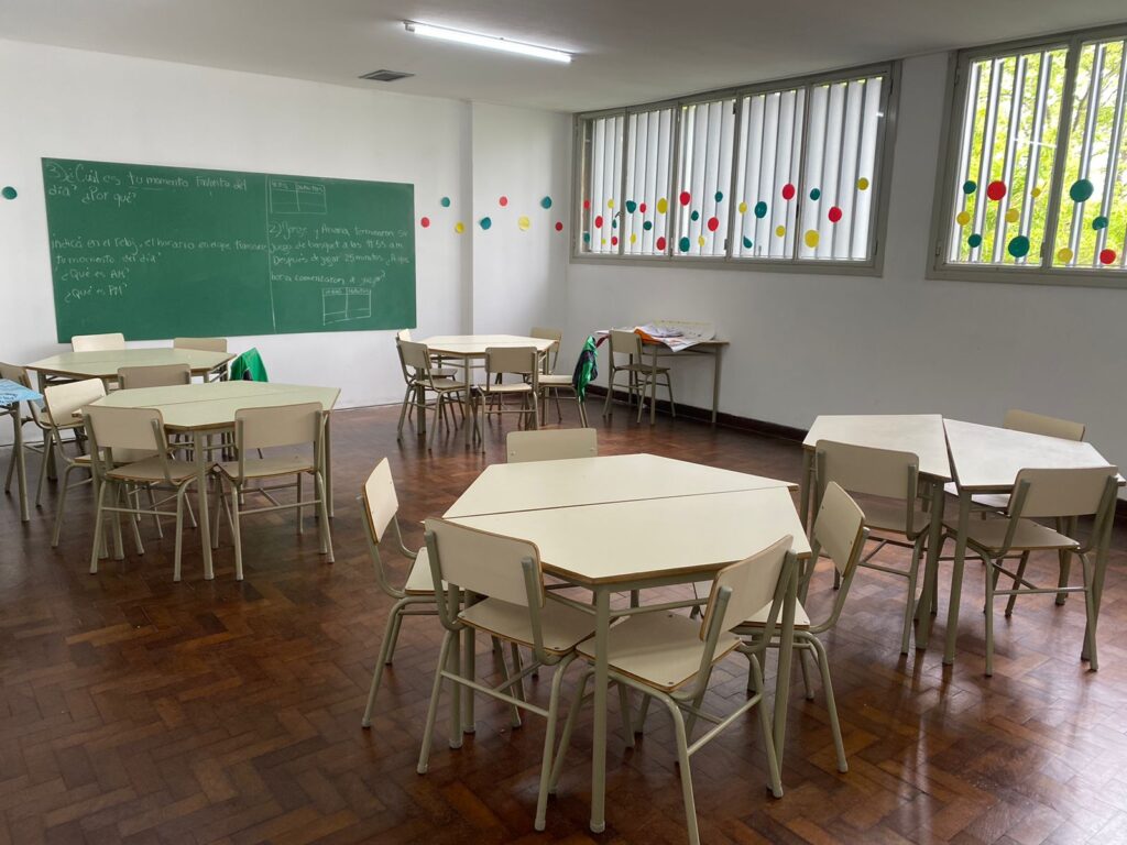 Aula escolar con mesas y sillas, pizarra con texto. Ambiente de aprendizaje para "Experiencia".