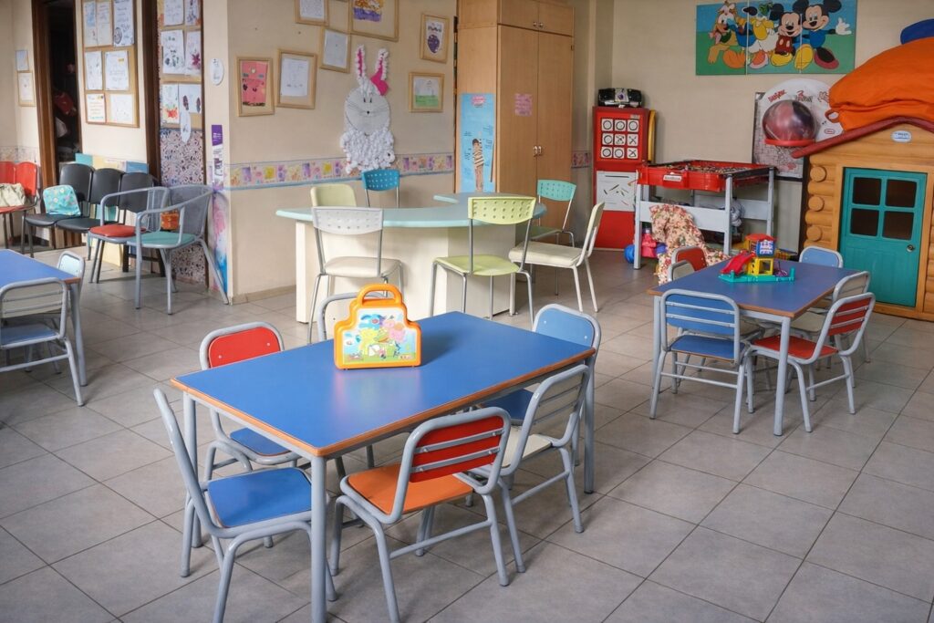 Aula infantil con mesas y sillas de colores, juguetes y dibujos en la pared.